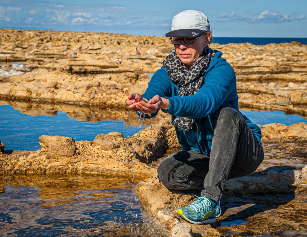 Angela Berg schöpft das salzhaltige Wasser aus einer antiken Salzpfanne / © Foto: Georg Berg