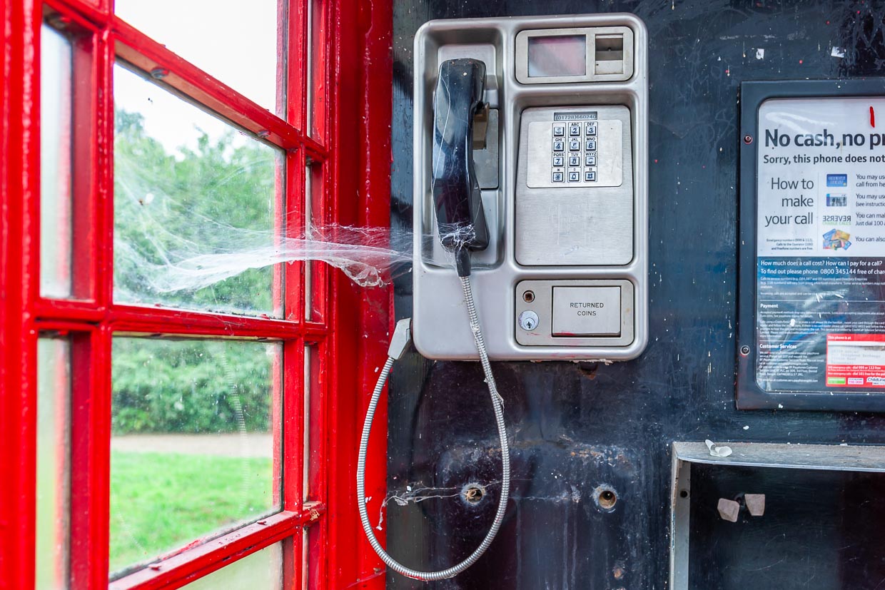 Eine traditionelle rote Telefonzelle in einer ländlichen Umgebung im Vereinigten Königreich zeigt ein Spinnennetz über dem Hörer / © Foto: Georg Berg