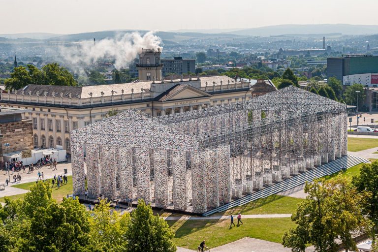 Parthenon der Bücher, der argentinischen Künstlerin Marta Minujin auf der  documenta 14 in Kassel. Täglich wurde die Konstruktion, die in ihrer Dimension ein Nachbau des Tempels auf der Akropolis ist, massiver und mit weiteren Büchern bestückt. Im Hintergrund raucht die Installation "Expiration Movement" im Zwehrenturm. / © Foto: Georg Berg
