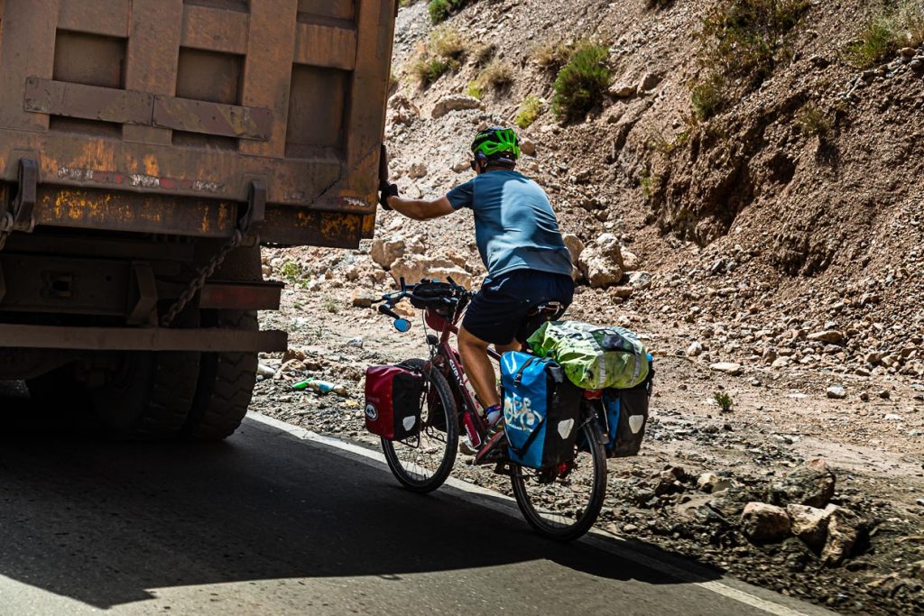 Ein Fahrradtourist lässt sich in Tadschikistan von einem LKW den Takfon-Pass hochziehen. Im Schlepptau von Transportern  lassen sich gerne mehrere Hundert Höhenmeter überwinden / © Foto: Georg Berg