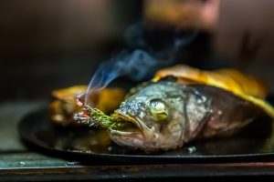 Der Loup de Mediterranée gefüllt mit einem zart getrüffelten Souffle von Cyril Aveline räuchert sich noch im Jospergrill selbst mit einem Rosmarinzweig / © Foto: Georg Berg