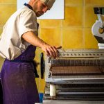 Mitarbeiter der Chocolaterie Frigoulettte in Beaufort-sur-Gervanne beim Zuschnitt von Nougat-Pralinen. Die geschnittene Praline kommt ohne eine zusätzliche Schokoladenhülle aus. Die Manufaktur verwendet ausschließlich biozertifizierte und fairtraide gehandelte Kakaobohnen aus São Tomé / © Foto: Georg Berg