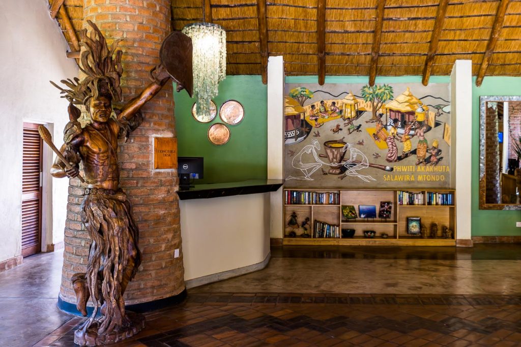 Eingangshalle Makokola Retreat am Lake Malawi bei Mangochi. Die große Figur zeigt den letzten Kämpfer der Ngoni, das Wandbild eine traditionelle Empfangsszene, wenn Gäste ein Dorf erreichen / © Foto: Georg Berg