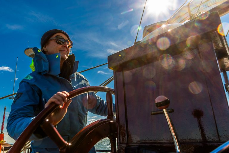 Kapitänin Jane Bothe steuert die Weisse Düne, ein holländisches Plattbodenschiff, durch das Achterwasser, die Lagune des Peenestroms, der in die Ostsee mündet. Mehrmals wöchentlich startet das Schiff von Neppermin, Wolgast oder Karlshagen zu Fahrten durchs Achterwasser / © Foto: Georg Berg