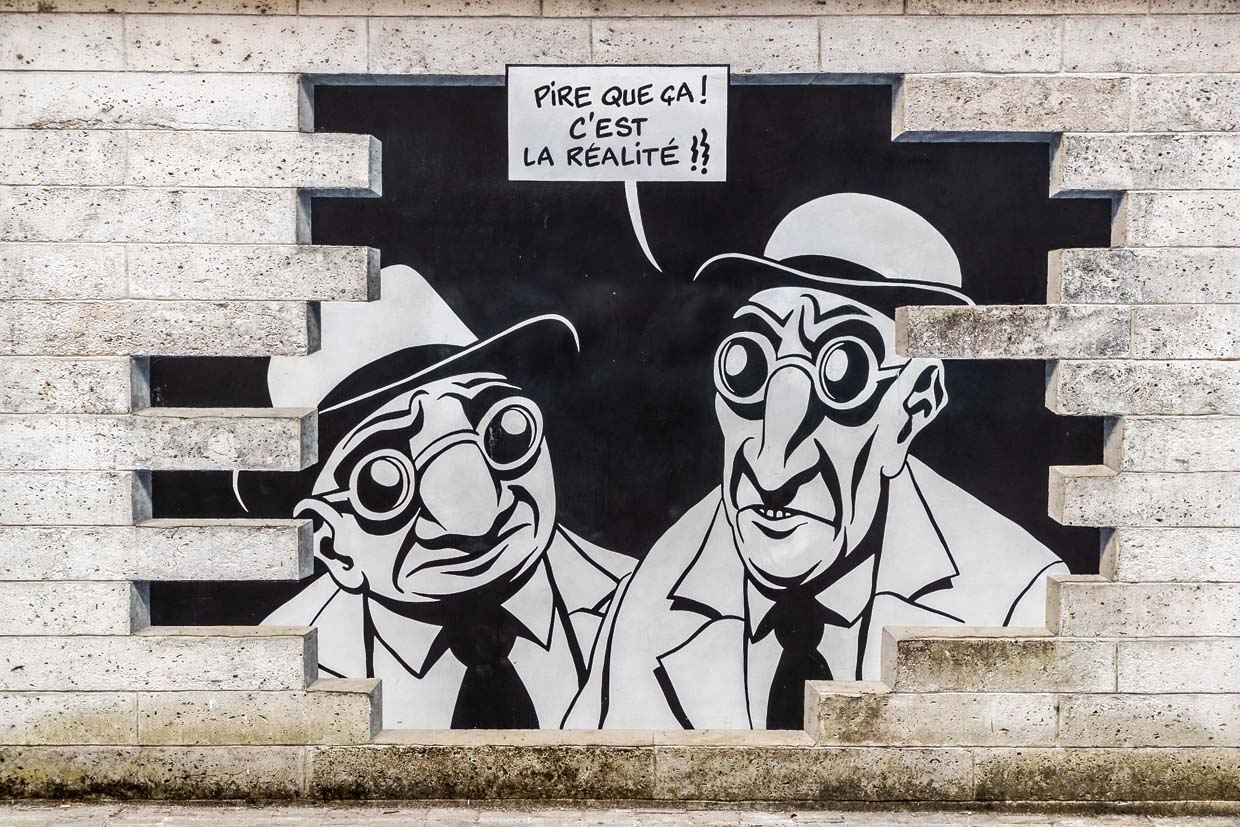 Wandgemälde aus der Serie „Réalité, Sortie de Secours” (Realität, Notausgang), die von Marc-Antoine Mathieu entworfen wurde. Es zeigt Comicfiguren mit Sprechblasen, die aus der Wand hervorzubrechen scheinen. "Sehen Sie etwas?" "Ja, schauen Sie. Es ist genau das, was ich befürchtet habe." "Was, schon wieder eine Unterwelt?" "Schlimmer als das. Es ist die Realität.".  / © Foto: Georg Berg