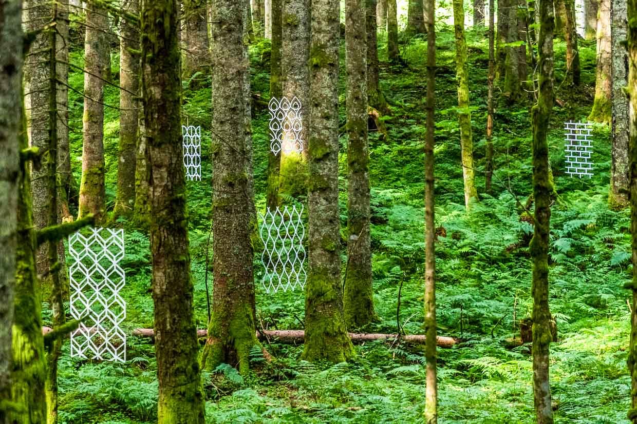 Naturkunstwerk „Durchblick“ von Susanne Ruoff aus Deutschland. Dünne Platten mit floralen und naturnahen Ornamenten freihängend zwischen Bäumen. Landart Pfad Gerschnialp in Engelberg 2025 / © Foto: Georg Berg