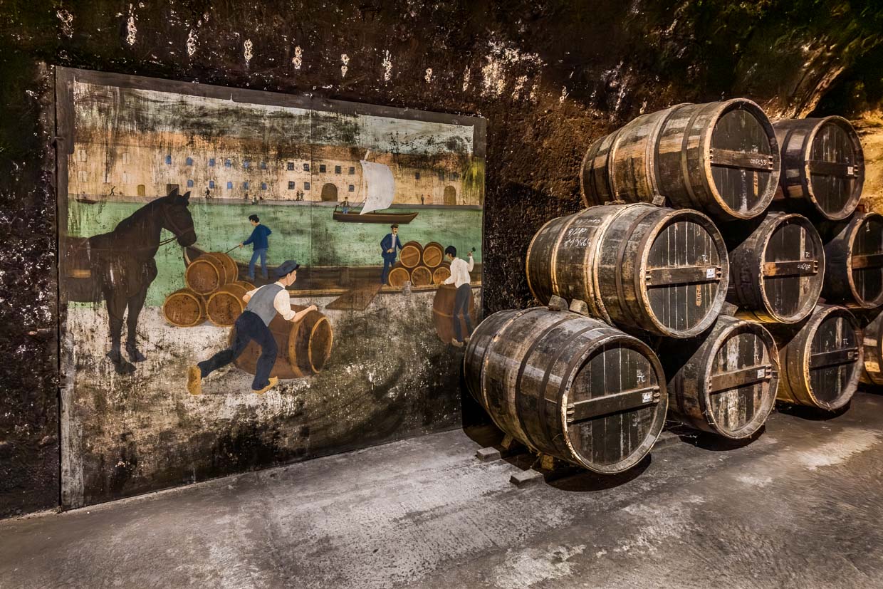 Old cognac barrels in the storerooms of Cognac Castle. Next to it, a painting depicting the trade in cognac and transportation across the Charente River / © Photo: Georg Berg