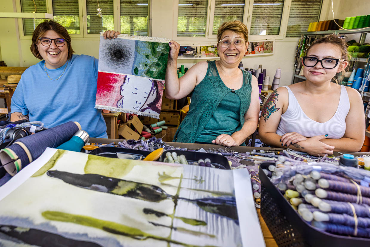 Sarah Chassain, Teamleitung für das Projekt Wandteppich "Hommage à George Sand“ im Atelier Robert Four mit den Kolleginnen Frederique und Agathe. Sie halten das Musterstück hoch, mit dem sie sich für Ausschreibung beworben haben. Das Musterstück zeigt auf kleiner Fläche verschiedenen Fertigkeiten, die ein Team für die Realisierung des Teppichs beherrschen muss / © Foto: Georg Berg