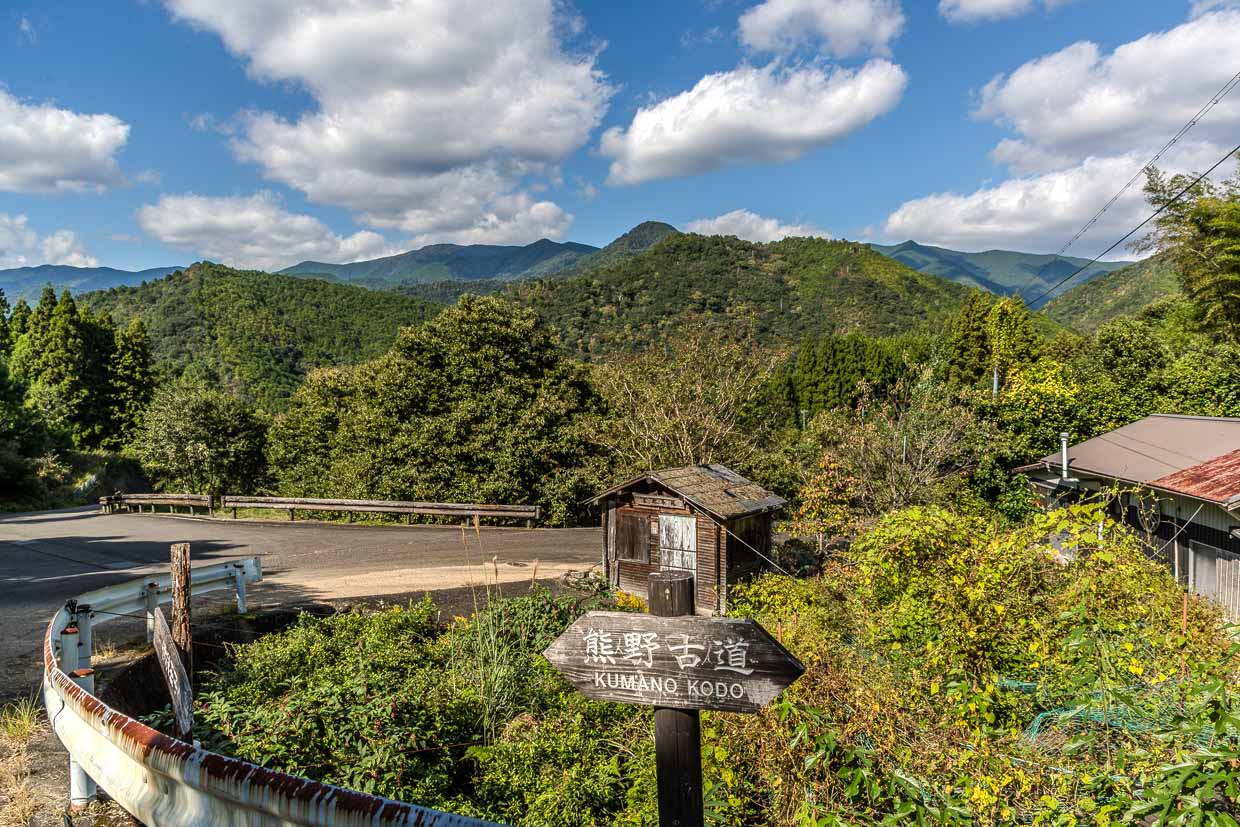 Wegweiser zum Pilgerweg Kumano Kodo an einer Straße. Blick in die Hügellandschaft mit dichten Zedern- und Zypressenwäldern / © Foto: Georg Berg