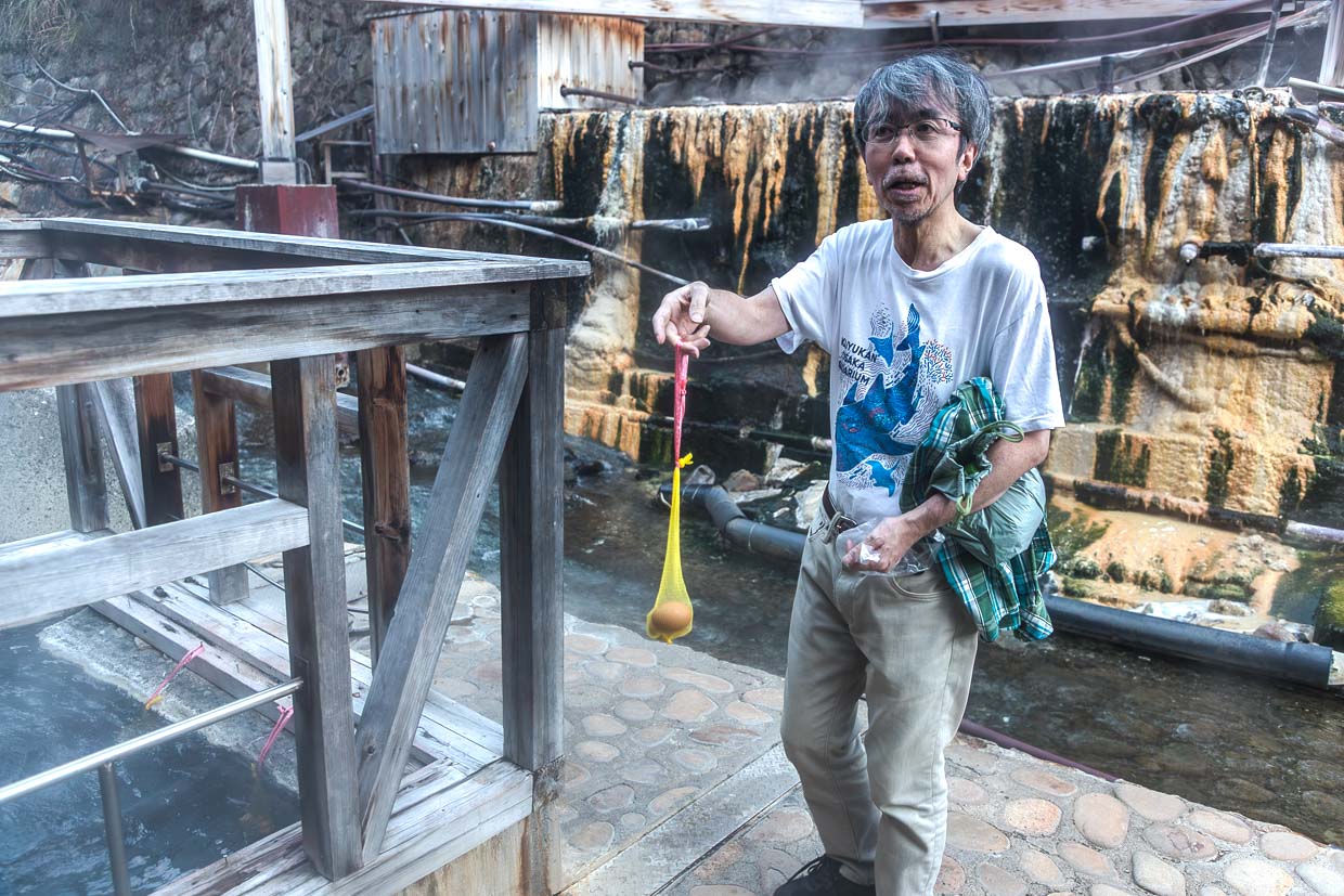 Am Flussufer in Yunomine Onsen befindet sich ein Becken mit etwa 90 °C heißes Quellwasser. Dort kann man Eier und Gemüse in Körben oder Netzen kochen. Hier ein japanischer Tourist mit rohen Eiern in einem Kunststoffnetz / © Foto: Georg Berg
