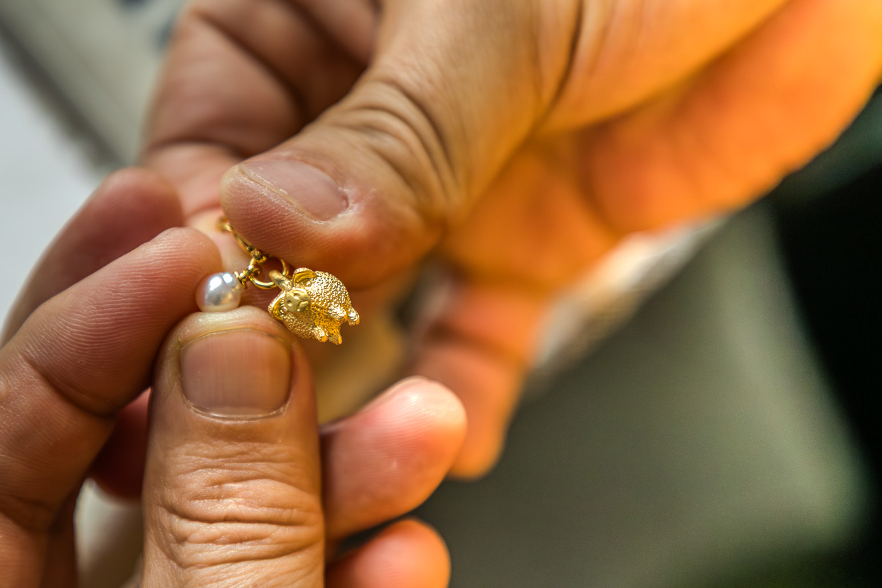 Hände halten ein goldenes Schweinchen-Schmuckstück mit Perle in Shima, Japan
