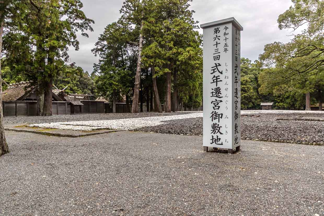 Japanisches Schild steht auf Kiesfläche vor traditionellen Holzhäusern und Bäumen in Miyajiri 1-chome, Ise, Japan