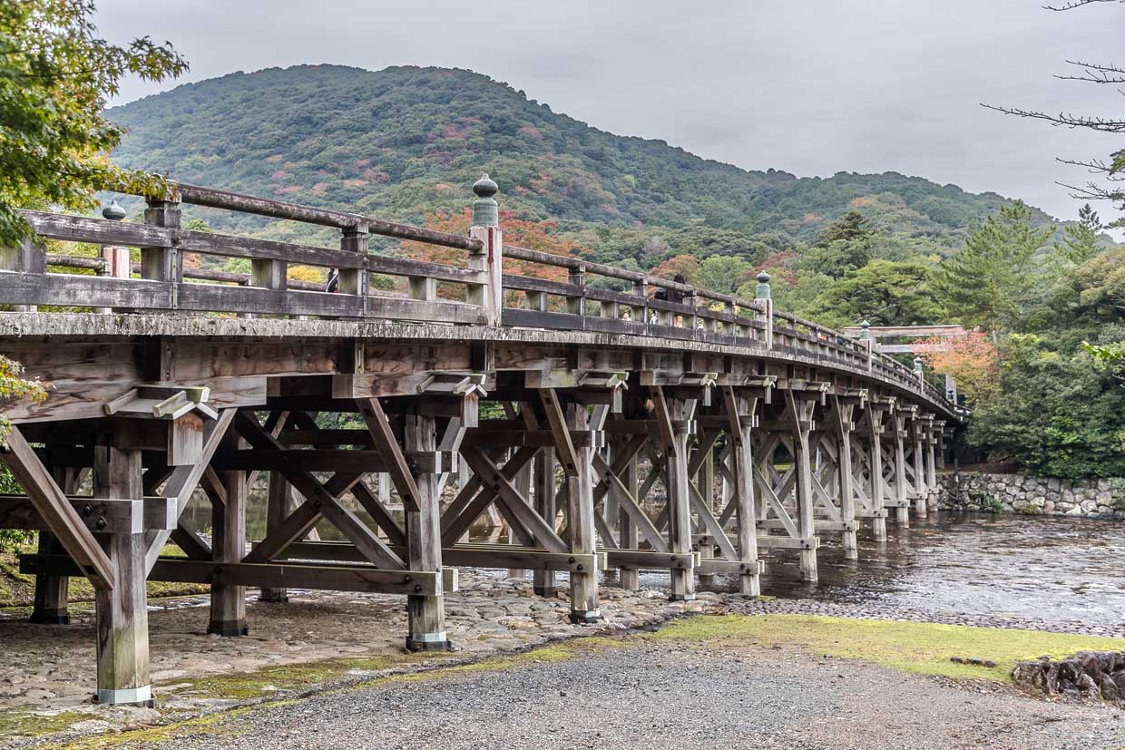 Die historische hölzerne Fire bridge überspannt einen Fluss vor einer bewaldeten Hügellandschaft in Ise, Japan