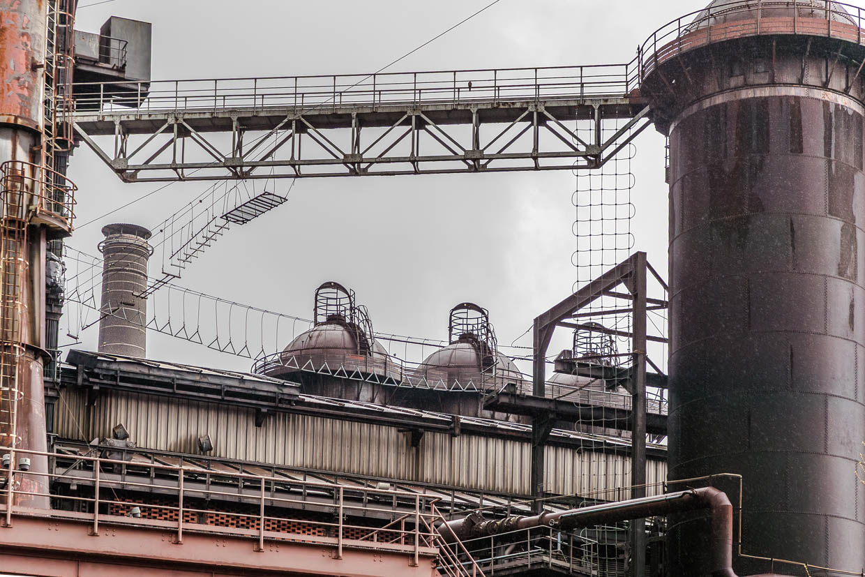 Blick auf einen Teil des Hochseilgartens „Expedition Stahl“. Zwischen zwei stillgelegten Hochöfen spannt sich in 55 Metern Höhe ein Parcours mit Seilen, Brücken und Plattformen über eine ehemalige Gießhalle. Er bietet Kletterspaß in Industriehöhe und endet mit Ausblick auf den Park / © Foto: Georg Berg