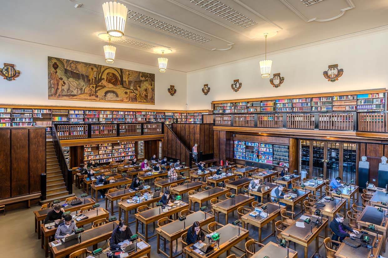 Der erste Lesesaal in der Deutschen Nationalbibliothek Leipzig mit grünen Leselampen und grüner Linoleum Arbeitsfläche. An den Wänden befinden sich Fresken mit Spätnazarener-Motiven / © Foto: Georg Berg