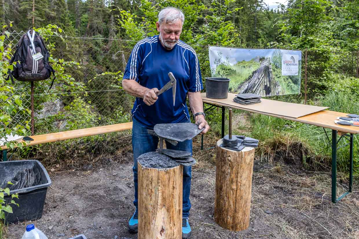 Älterer Mann bearbeitet Schieferplatten mit einem Schieferhammer im Geopark Schieferland an der Bergstraße in Ludwigsstadt Germany
