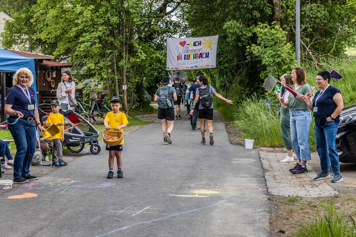 Wanderer passieren jubelnde Helfer und Kinder mit Süßigkeiten unter einem Willkommensbanner am Glasersteig, Steinbach am Wald