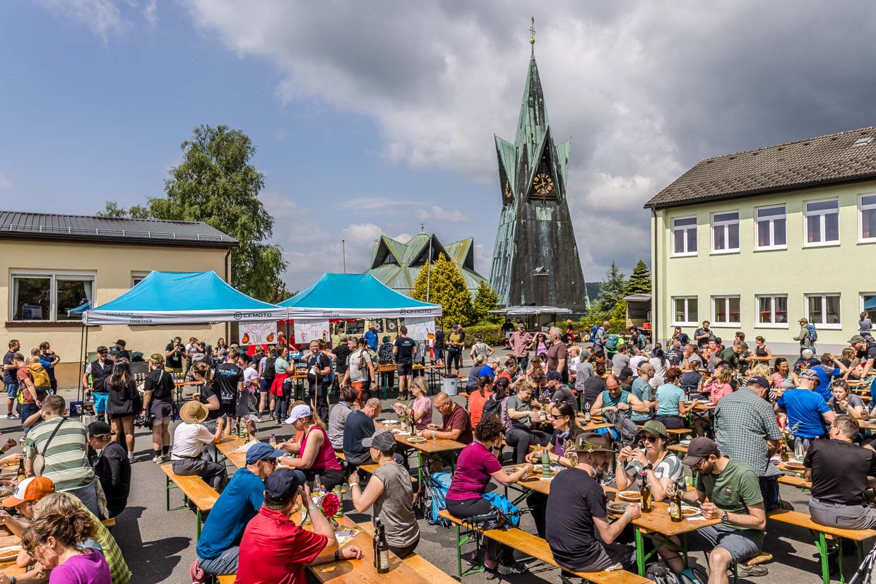 Zahlreiche Besucher essen und trinken an Biertischen vor der markanten Kirche in der Laurentiusstraße, Steinbach am Wald, Germany