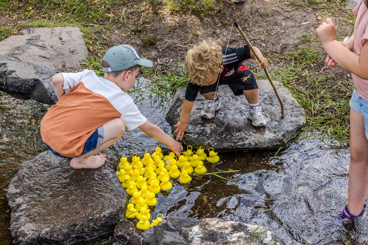 Zwei Jungen spielen mit gelben Quietscheentchen in einem Bach in Pressig Germany