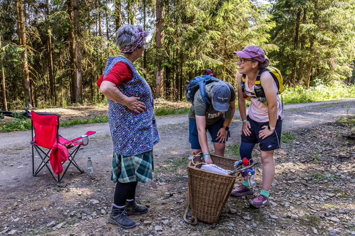 Eine ältere Frau präsentiert zwei Wanderern einen Weidenkorb auf einem Waldweg in Steinbach am Wald Germany