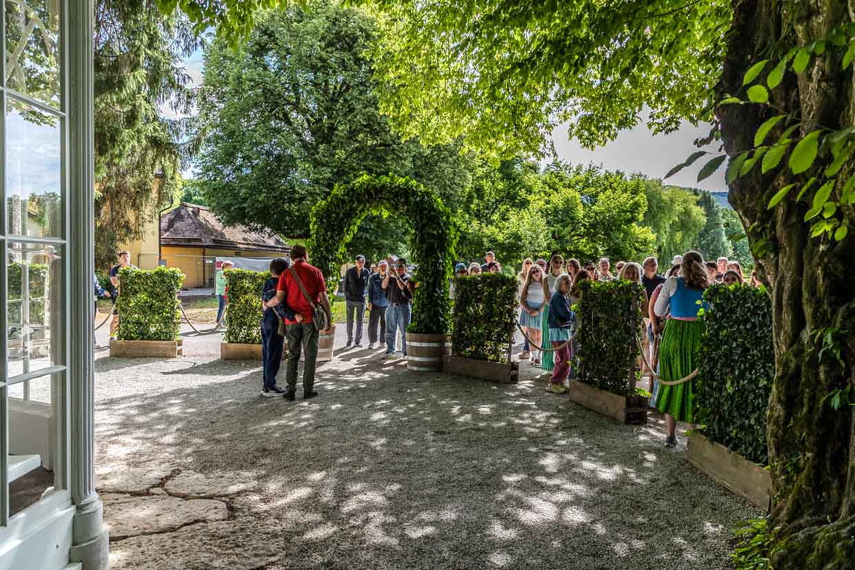 Eine Gruppe Menschen steht auf einem Kiesweg unter einem grünen Bogen und Bäumen am Fürstenweg, Salzburg, Austria