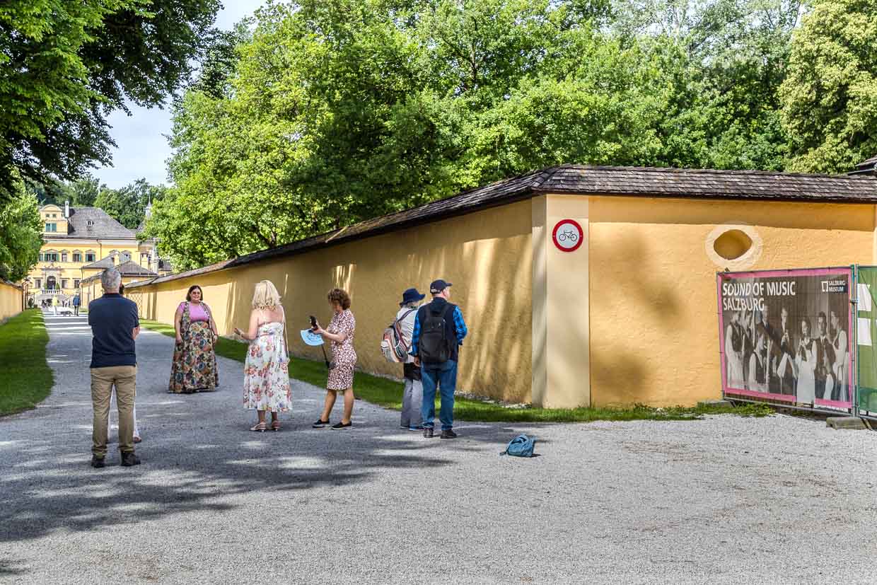 Besucher spazieren auf dem Fürstenweg in Salzburg Austria entlang einer gelben Mauer und einem historischen Schloss mit Sound of Music Banner