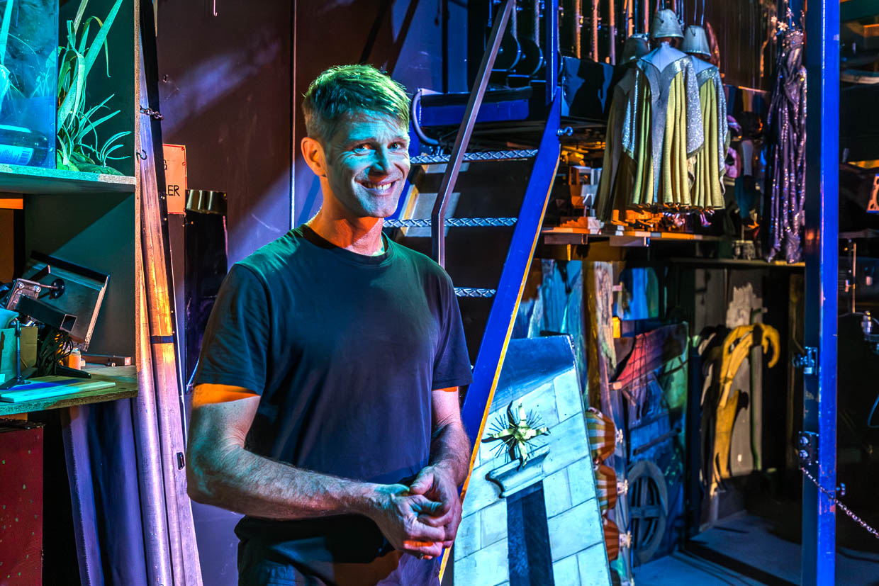 Ein lächelnder Mann steht inmitten von Theaterrequisiten und Kostümen in der Schwarzstraße, Salzburg, Austria