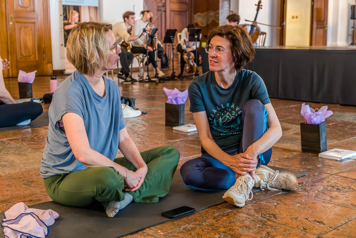 Zwei Frauen unterhalten sich während einer Veranstaltung auf Yogamatten am Domplatz, Salzburg, Austria, mit Live-Musik