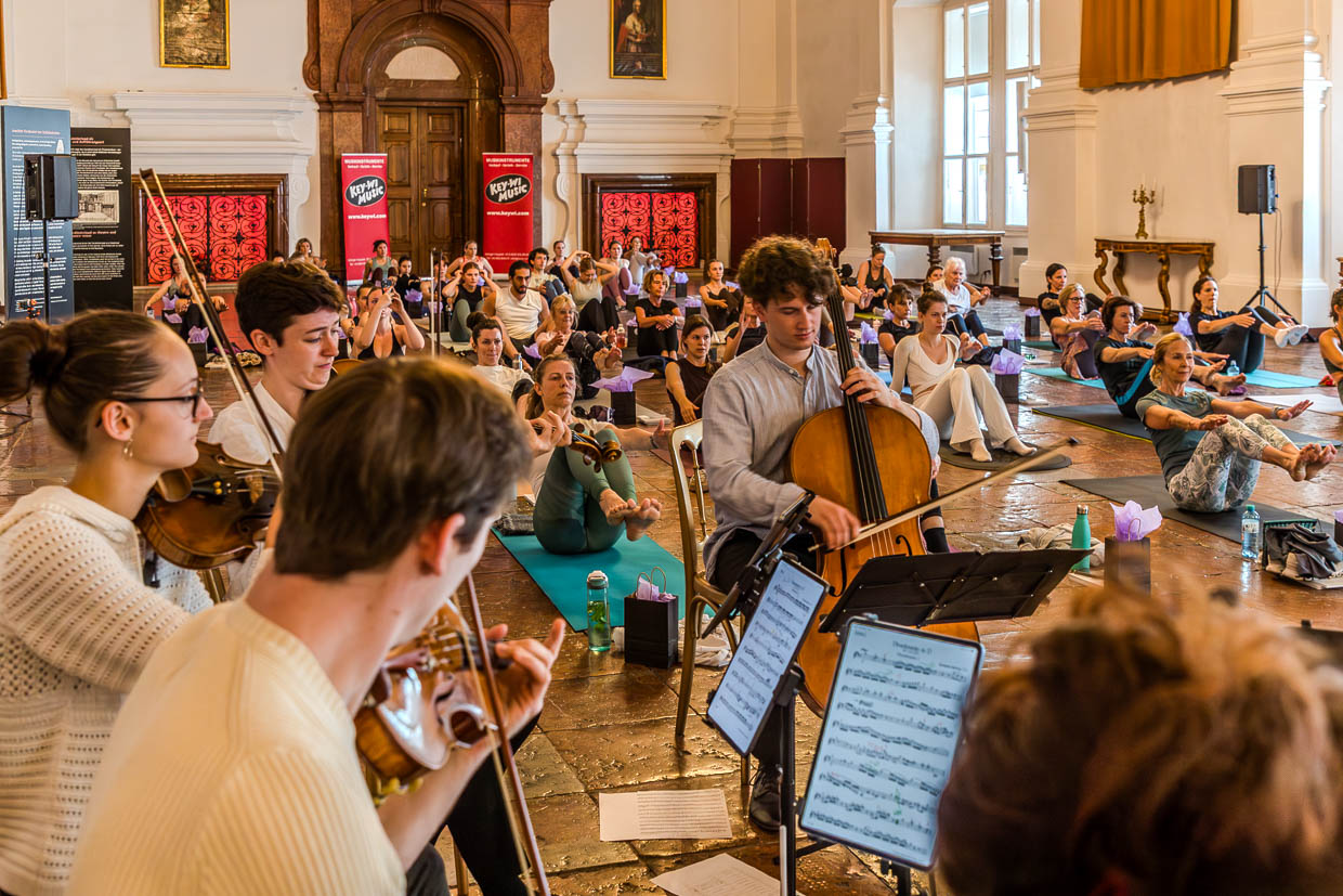 Junge Musiker spielen Streichinstrumente für Yoga-Praktizierende bei einem Event in der Franziskanergasse, Salzburg, Austria