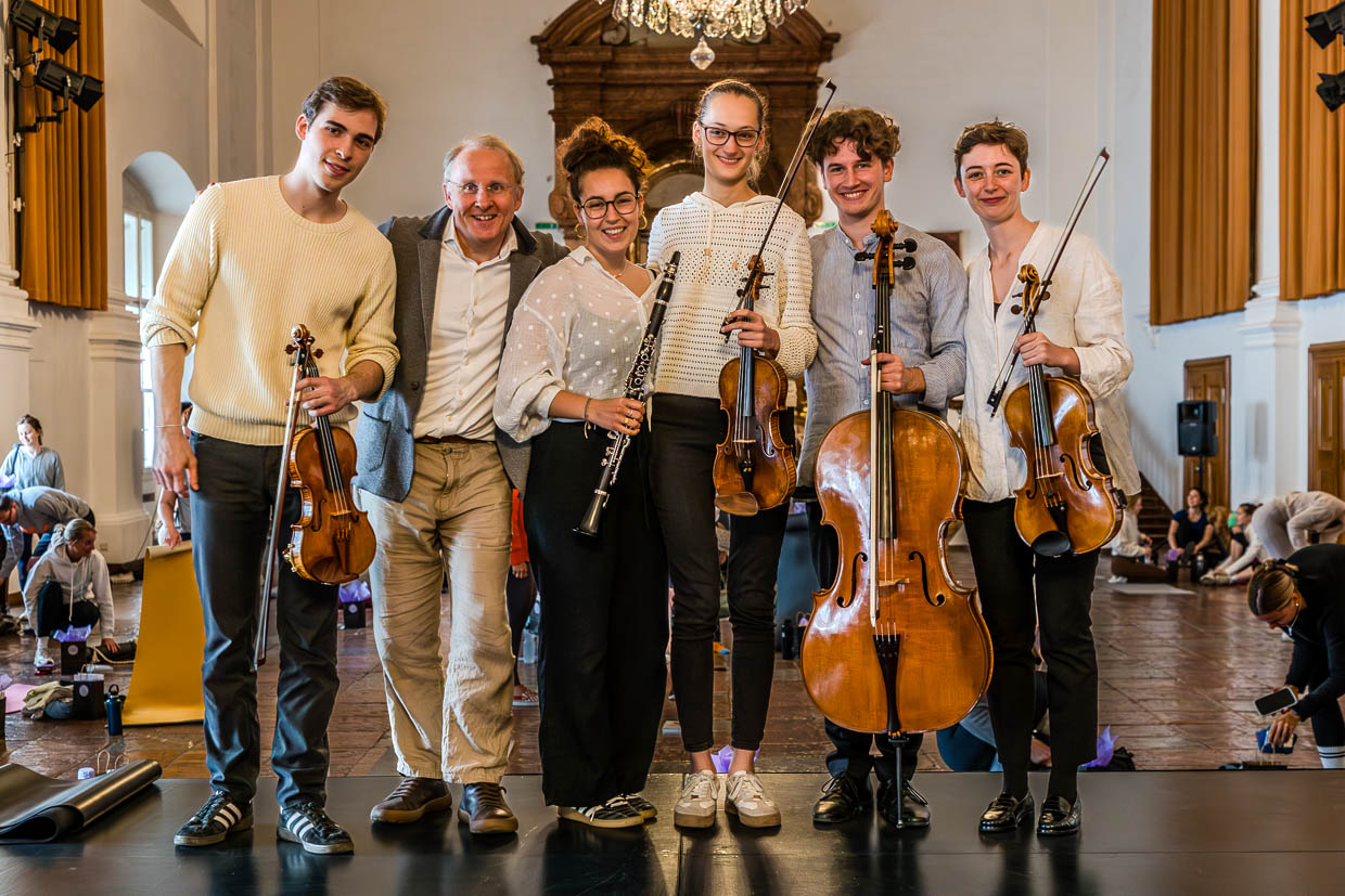 Ein Musikensemble aus jungen Musikern und einem älteren Mann posiert lächelnd mit Violinen, Cello und Klarinette in der Franziskanergasse, Salzburg, Austria