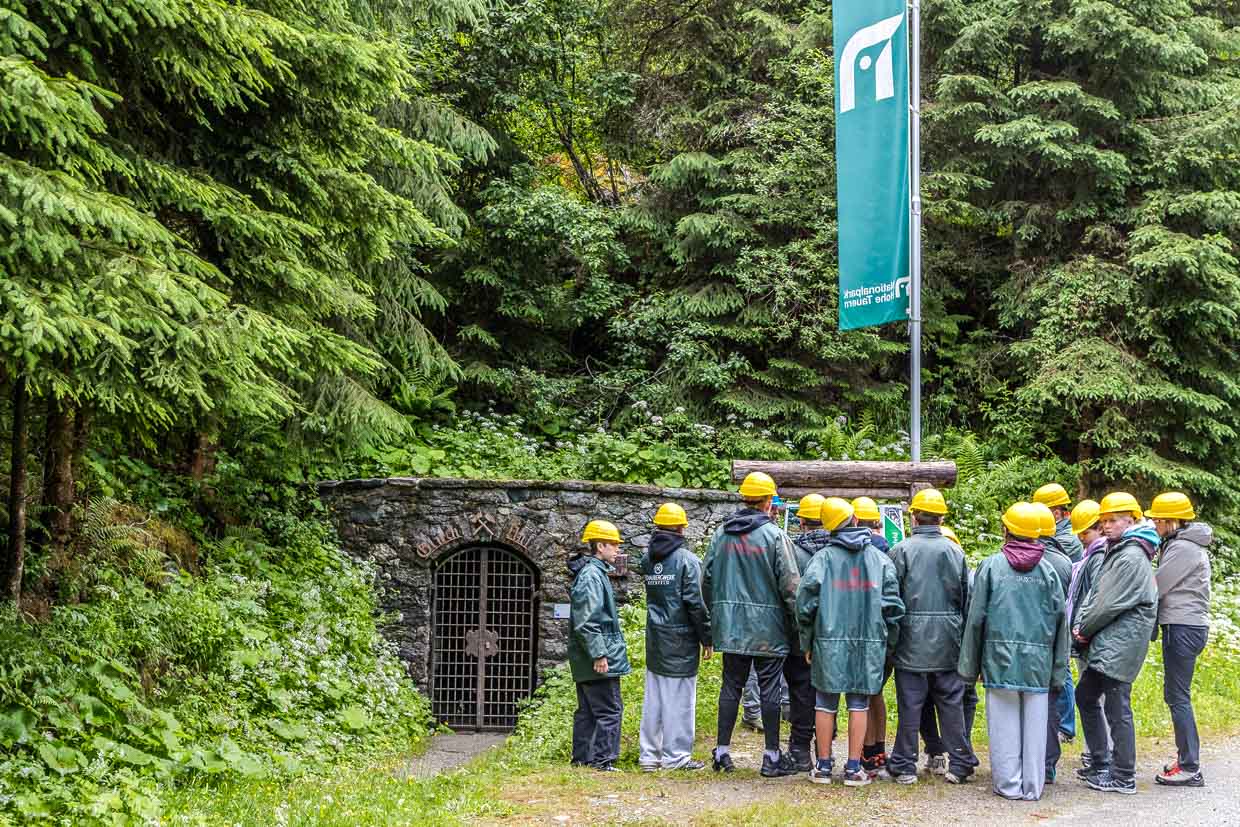 Besucher mit Helmen und Schaubergwerk-Jacken stehen vor dem Stollen "Glück Auf" am Wasserfallrundweg Untersulzbach Rosental Austria