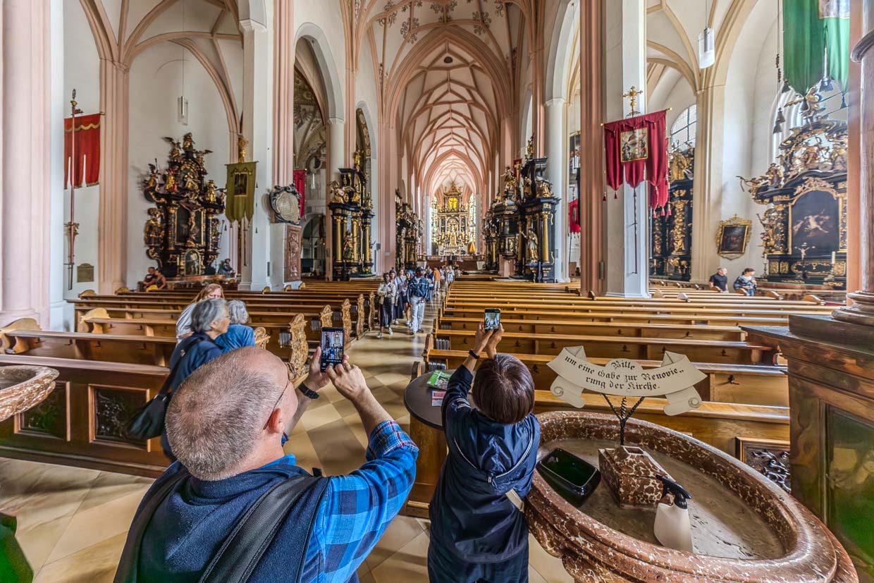 Besucher bewundern und fotografieren das historische Kirchenschiff mit prunkvollen Altären und hohen Gewölben in Poststraße Schlößl Austria