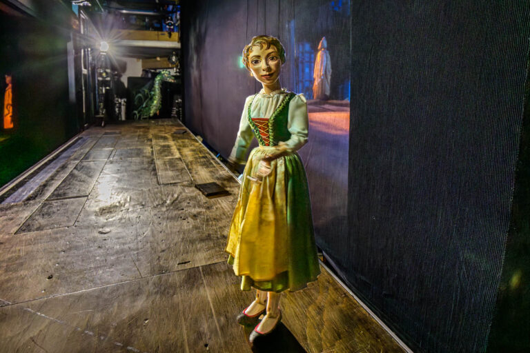 Eine beleuchtete Marionette im Dirndl steht vor einer Projektionswand auf einer Bühne in der Bristol-Passage, Salzburg, Austria