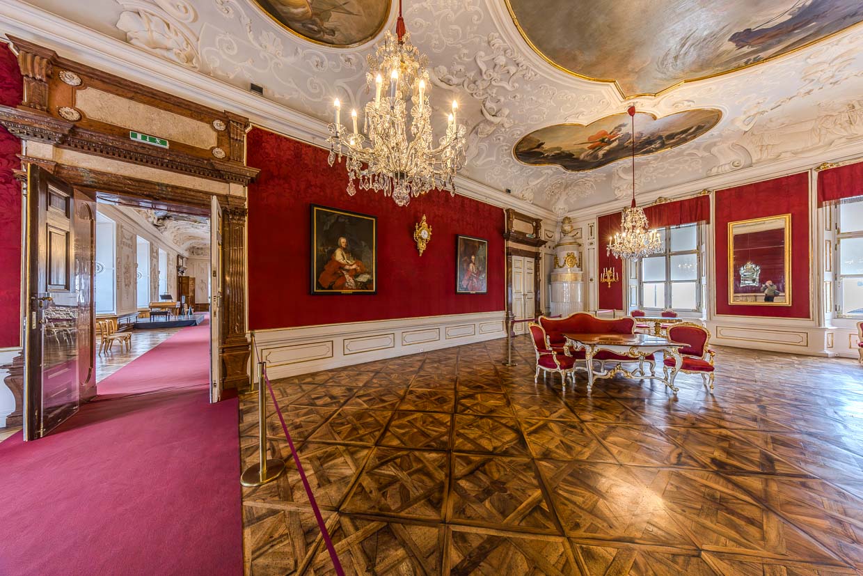 Ein opulenter Barocksaal mit roten Wänden, Deckenmalereien, Kronleuchtern und antiken Möbeln zeigt sich am Residenzplatz in Salzburg Austria