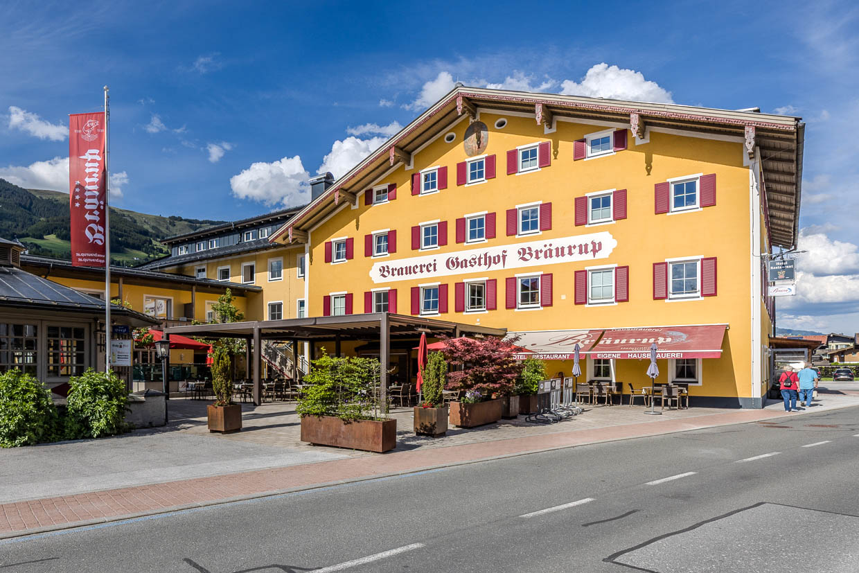 Die Kirchgasse in Mittersill, Austria, zeigt den gelben Brauerei Gasthof Bräurup mit Außenterrasse und zwei vorbeigehenden Personen
