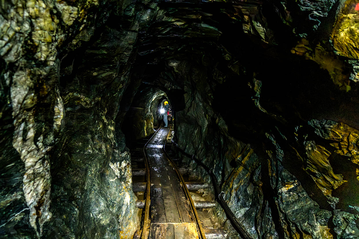 Ein Besucher mit Stirnlampe beleuchtet einen dunklen Bergbaustollen am Wasserfallrundweg Untersulzbach Rosental Austria