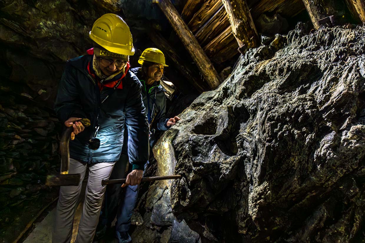 Zwei Personen mit Schutzhelmen erkunden einen Stollen mit Werkzeugen am Wasserfallrundweg Untersulzbach, Rosental, Austria