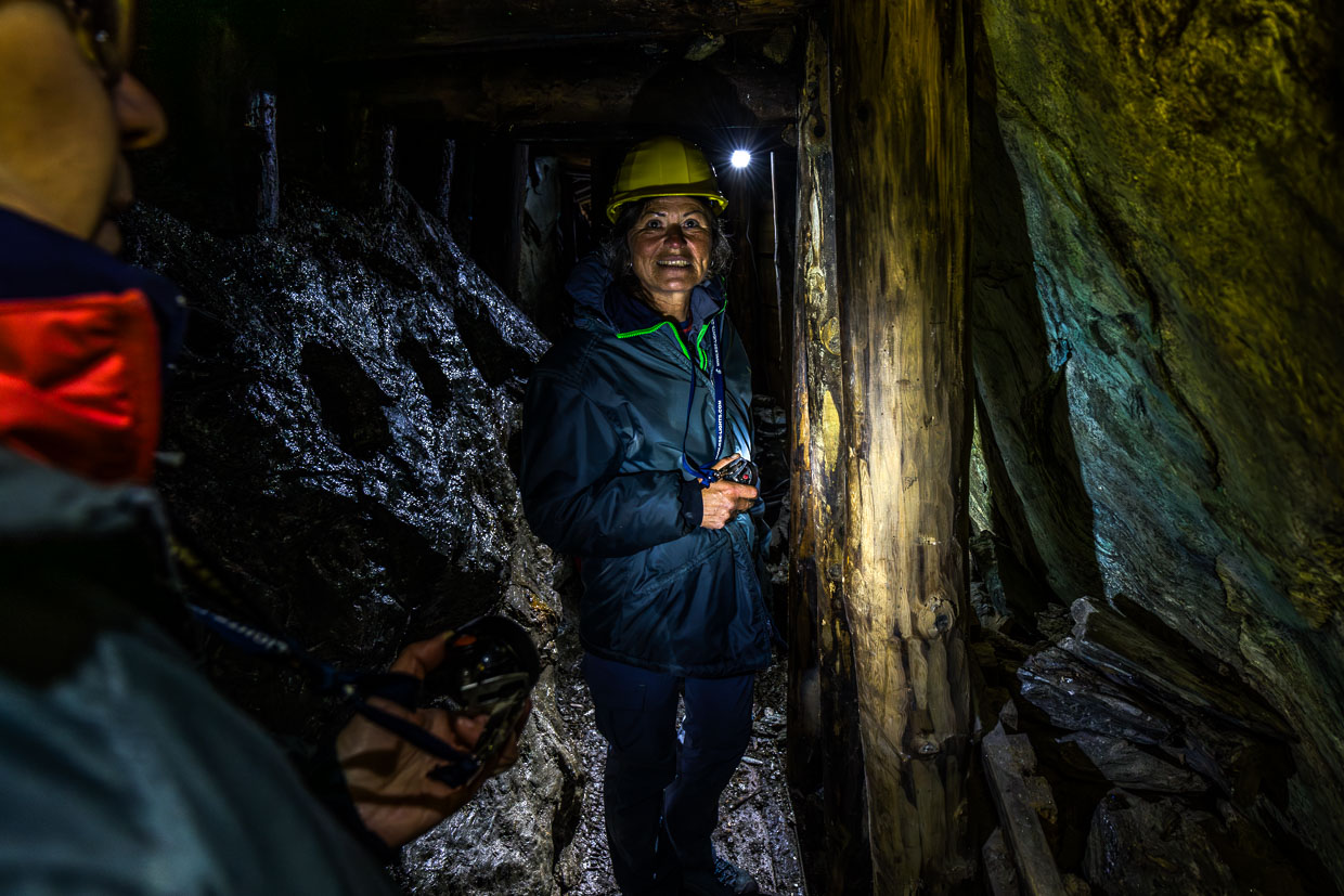 Eine lächelnde Frau mit Schutzhelm und Stirnlampe erkundet einen dunklen Stollen am Wasserfallrundweg Untersulzbach, Rosental, Austria