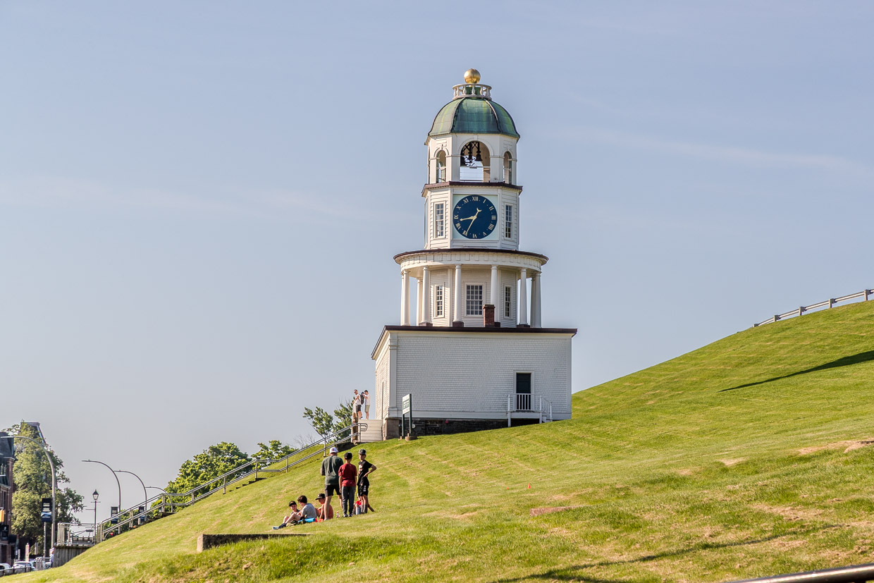 Menschen entspannen sich auf einer grünen Wiese vor dem Uhrturm am Halifax Waterfront