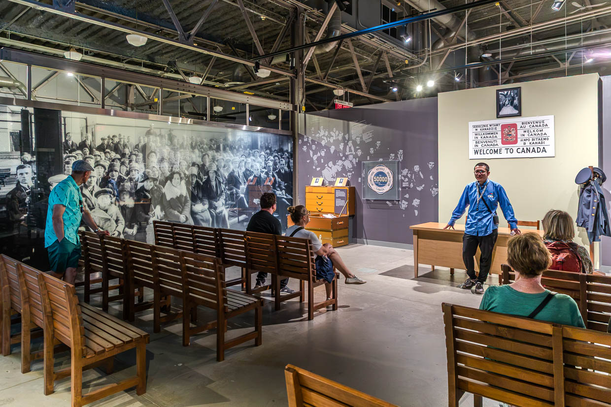 Ein Mann in blauem Hemd spricht zu Besuchern in einer Ausstellung über Einwanderung in Halifax, Kanada