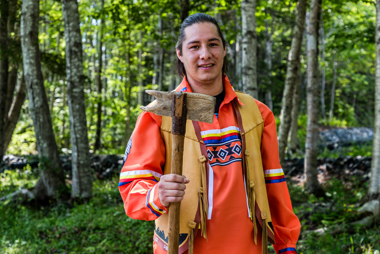 Ryan in traditioneller Kleidung hält eine Axt auf dem Goat Island Trail, Eskasoni First Nation, Canada
