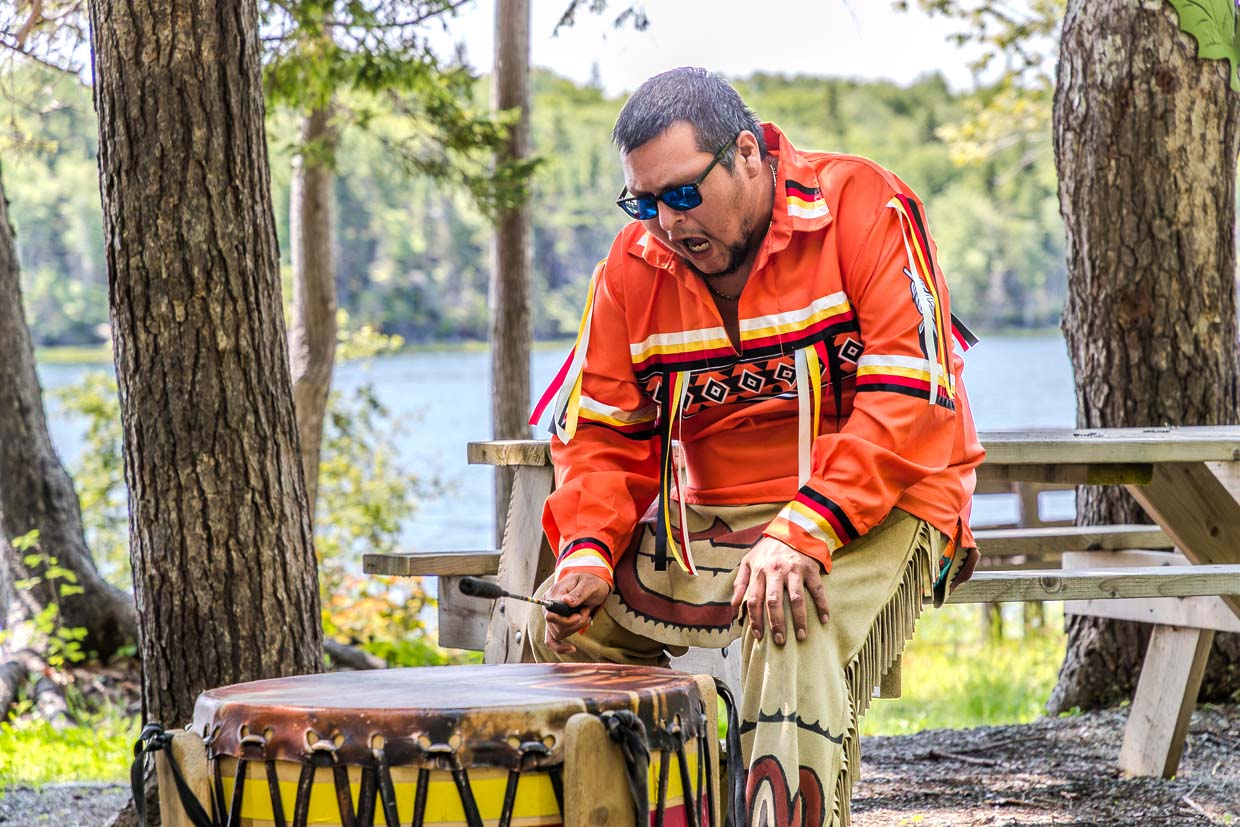 Mann in traditioneller Kleidung spielt Trommel am Goat Island Trail, Eskasoni First Nation, Canada