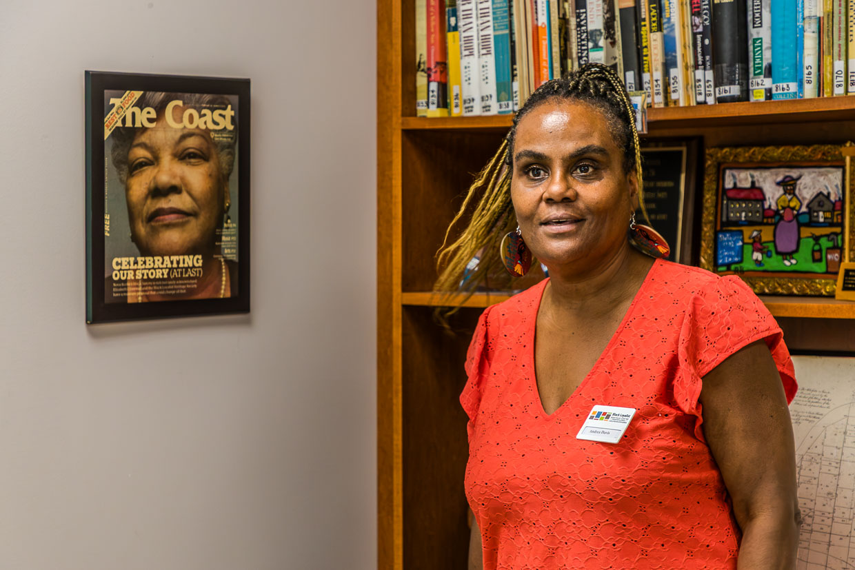Andrea Davis steht vor einem Bücherregal mit einem Namensschild am Ort Birchtown Road, Municipality of the District of Shelburne, Canada