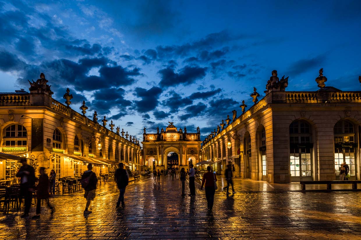 Menschen spazieren über den nassen Platz Stanislas in Nancy, Frankreich, bei Einbruch der Dunkelheit